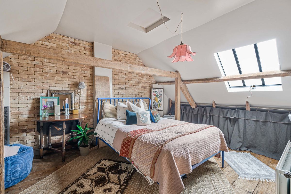 A second-floor bedroom under the roof, with exposed brick, a roof light and old timbers