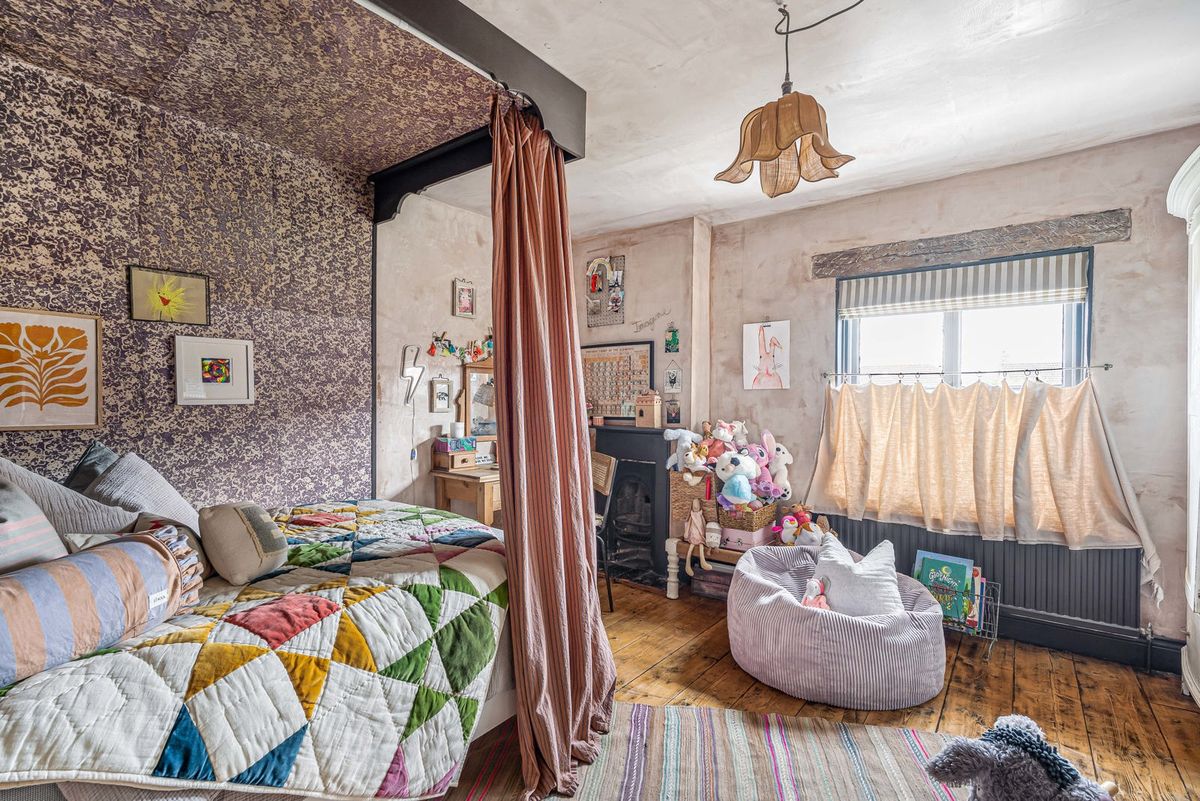 A bedroom with a canopied bed, patterned wallpaper and a window seat area