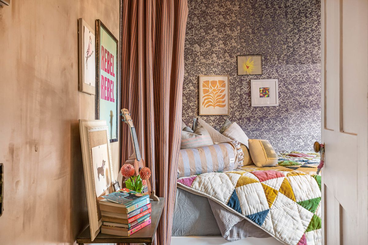 A quilt on the canopied bed and books stacked by the wall