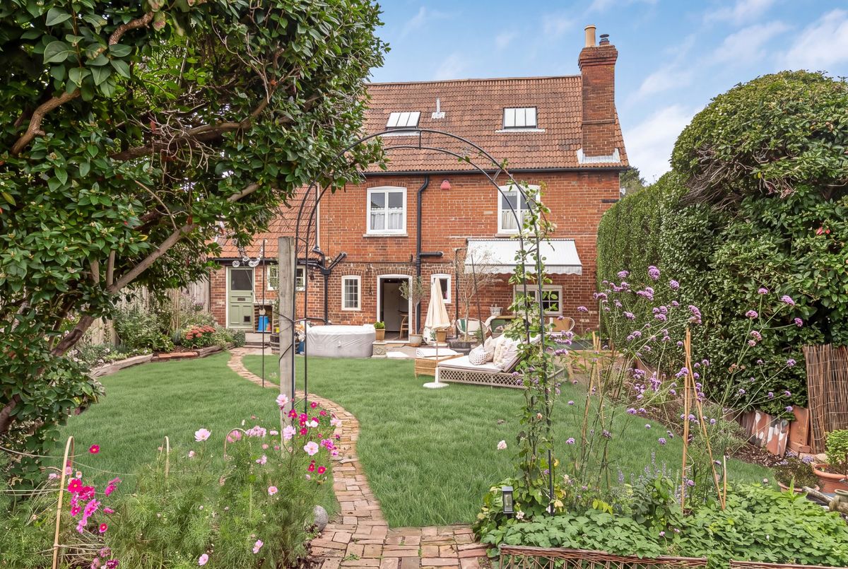 The rear garden in summer: a brick path winding through lawn and flowering borders towards the house