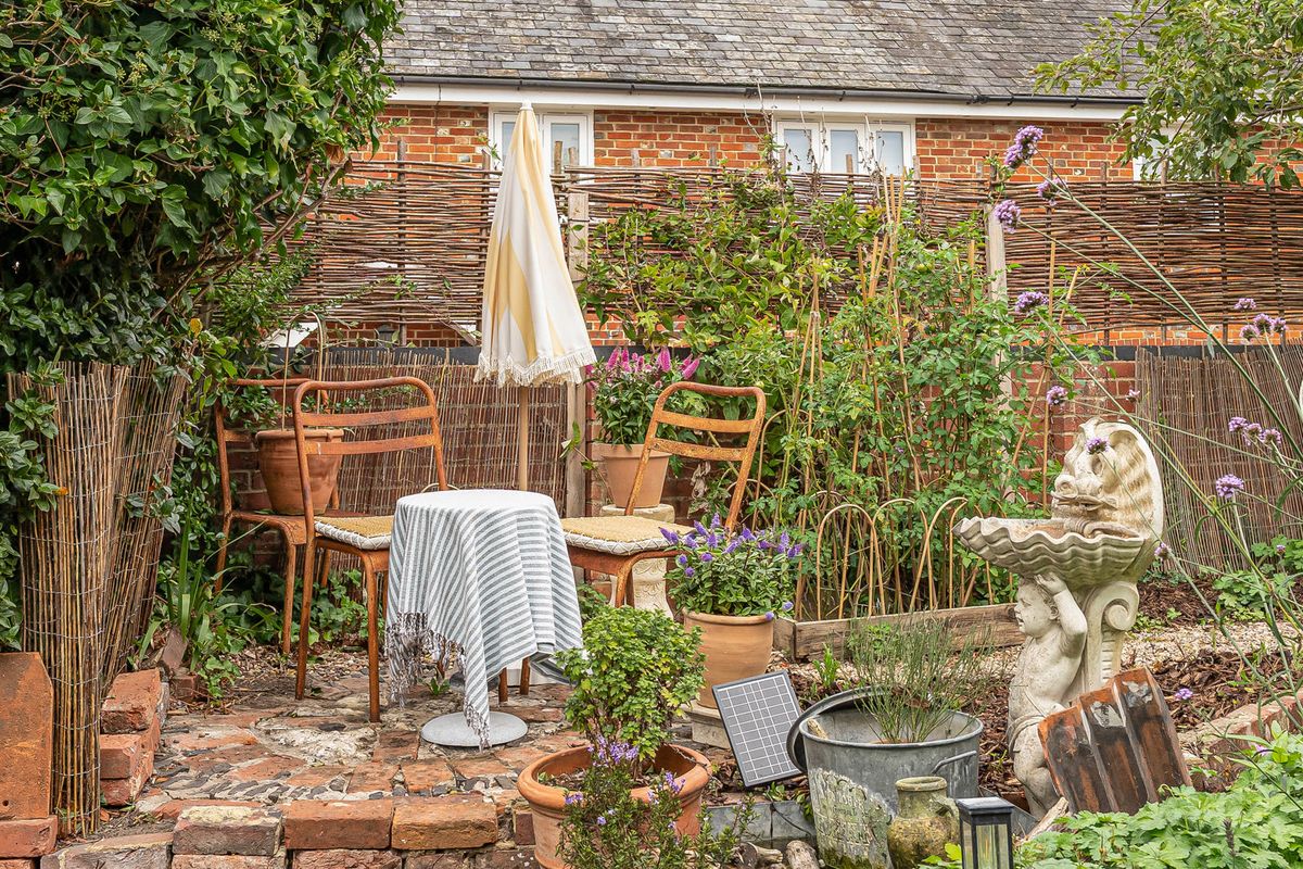 A small table and chairs among planting against a fence