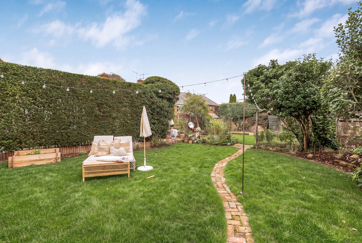 A brick path curving across the lawn beside a tall hedge