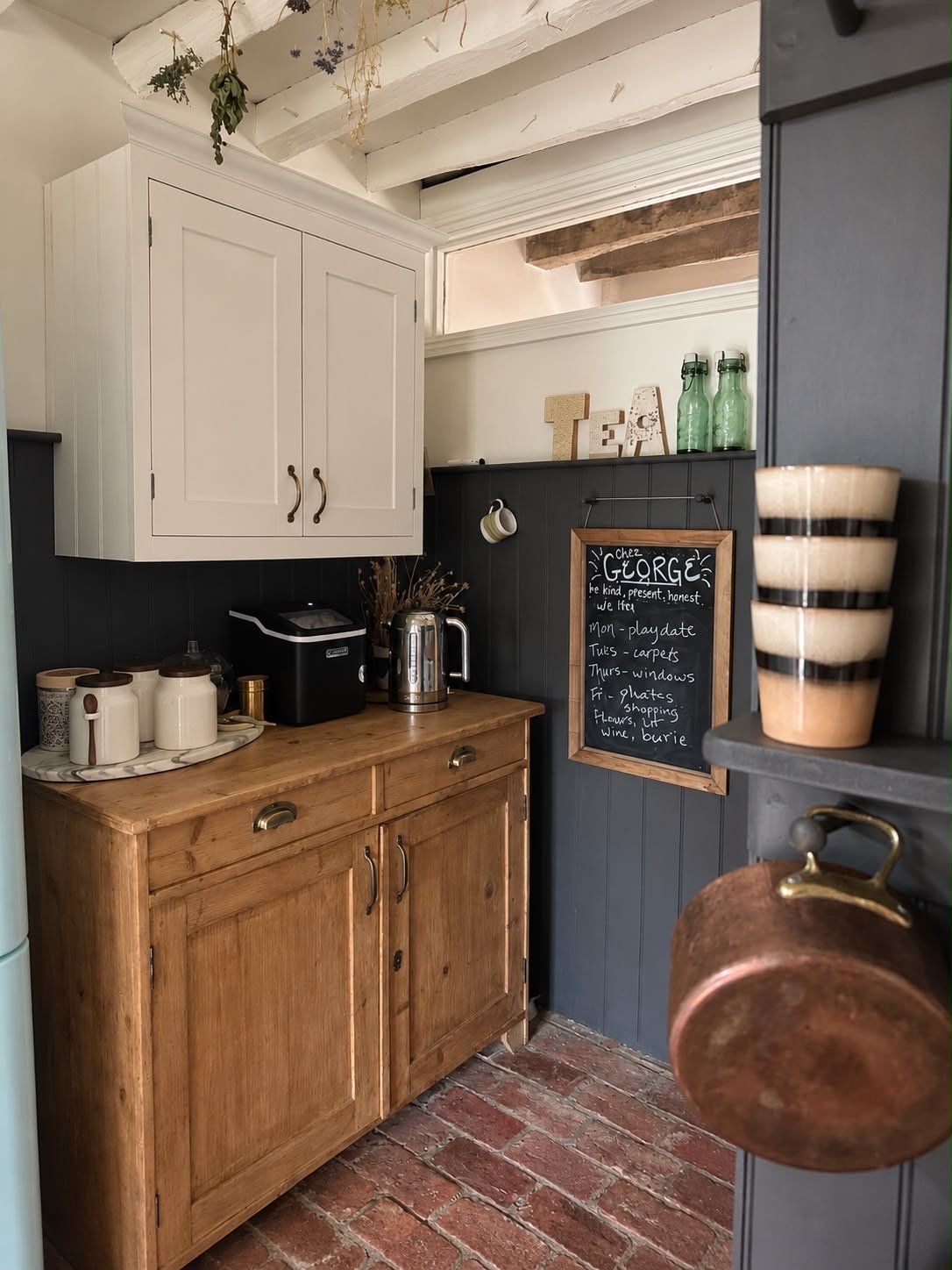 A pine cupboard, copper pan and a blackboard on a brick floor in the separated utility area
