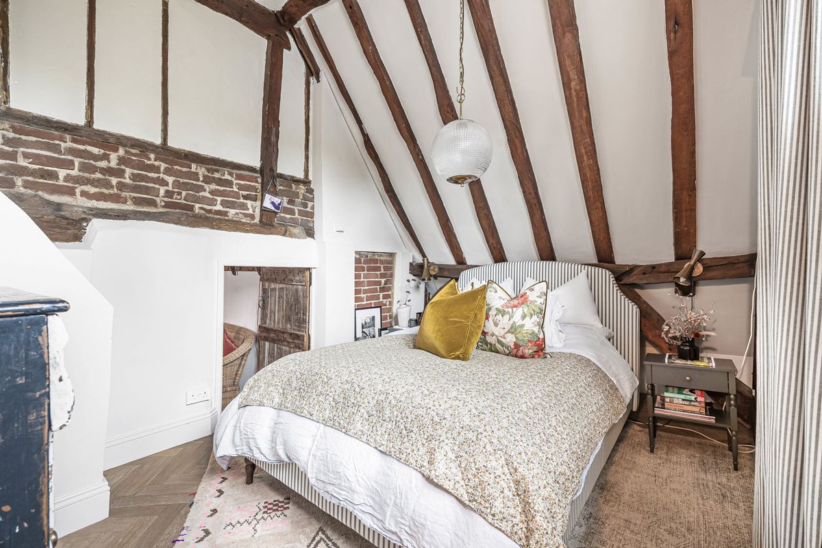 The principal bedroom beneath a vaulted ceiling of exposed beams, with a section of old brickwork
