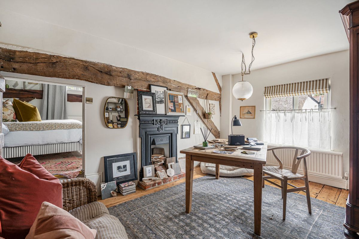 The study, with a cast-iron fireplace, a broad beam and a desk by the window; the principal bedroom visible through the doorway